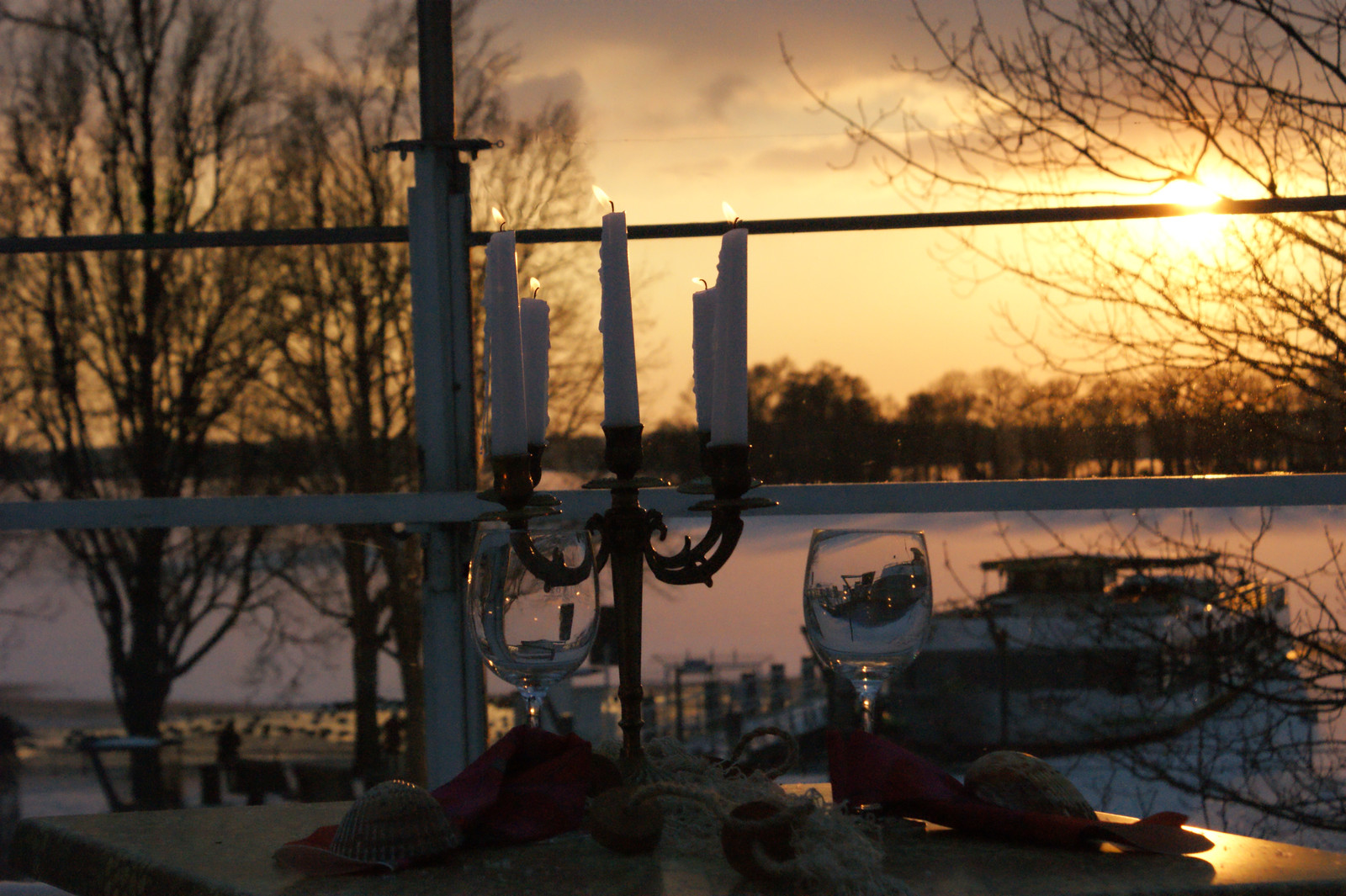 Kerzen und Weingläser am Fenster vor dem Tegeler See im Abendlicht