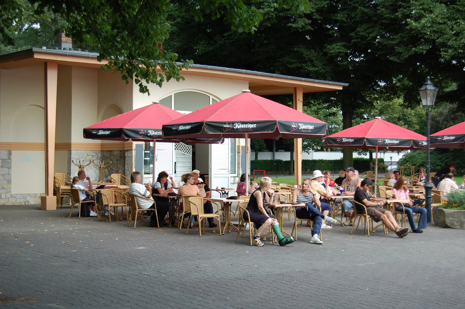 Pavillon am See mit Gästen unter roten Sonnenschirmen
