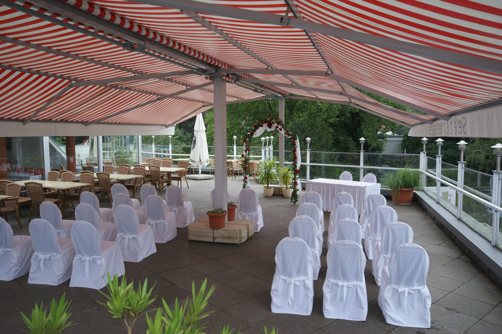 Terrasse mit weißen Stuhlhussen und Rosenbogen unter der Markise